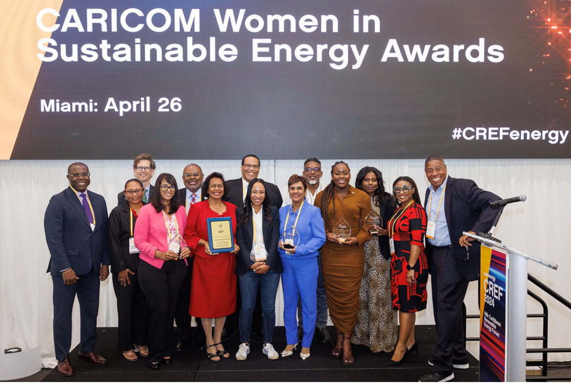 Several people stand on a stage below the words CARICOM Women in Sustainable Energy Awards 
