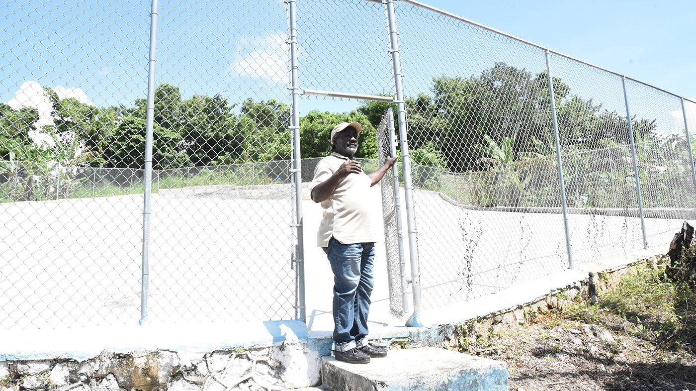 Trenail resident in white shirt and blue trousers stands at the open gate to water catchment facility