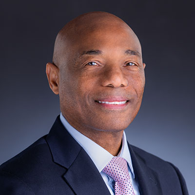 President Dr. Leon in black suit with white shirt and patterned lilac tie