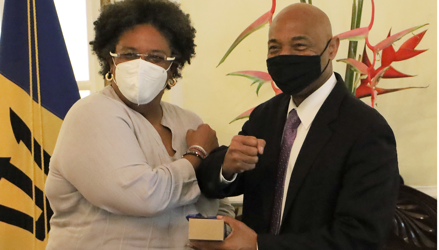 Barbados PM Mia Mottley in a beige jacket and CDB President Gene Leon in a dark suit, both with face masks, bump their wrists