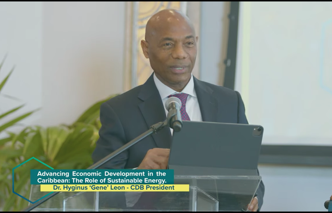 CDB President Dr Gene Leon in grey suit with purple tie addresses the TCI Energy Forum from a lectern