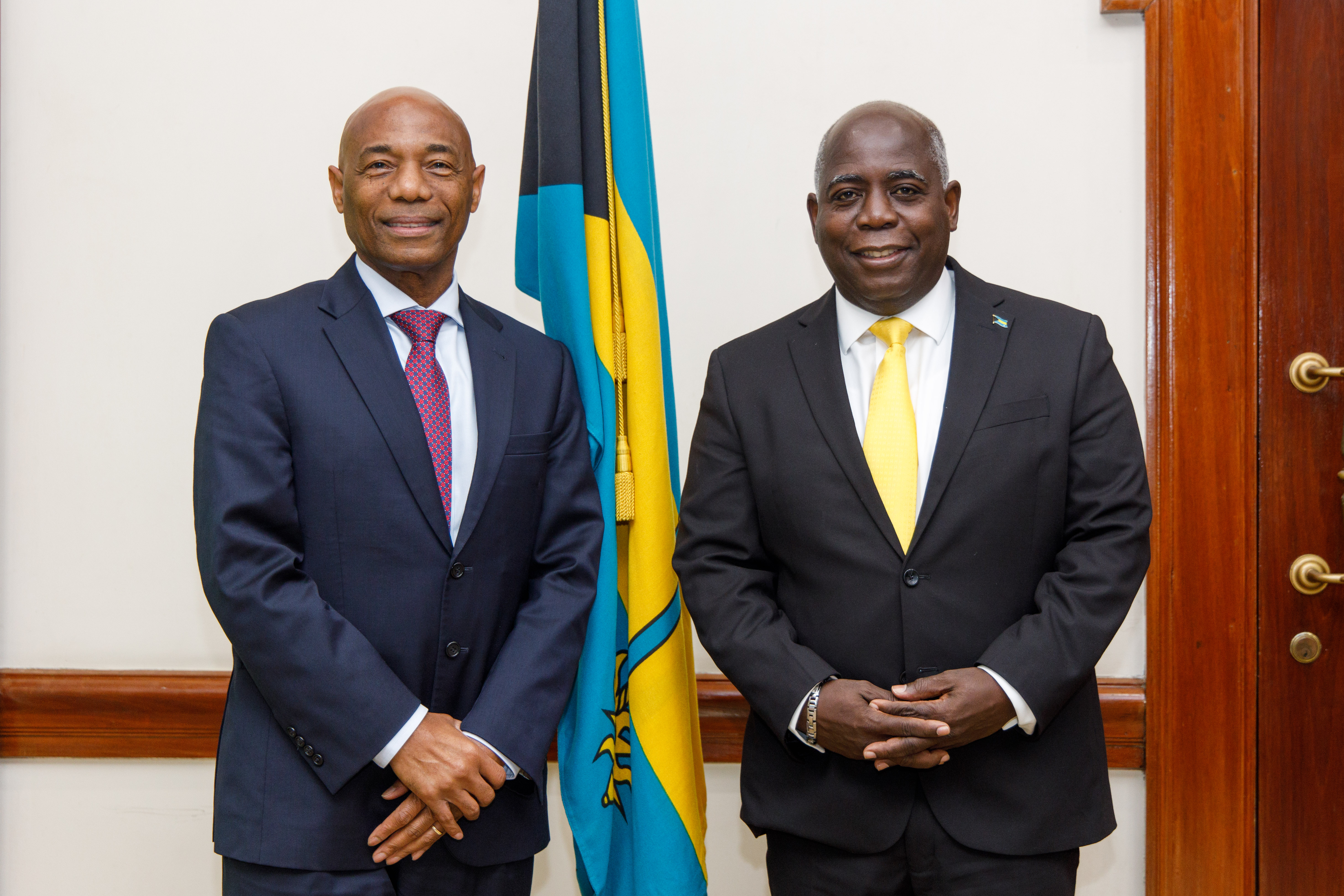 Dr. Gene Leon and the Honourable Philip Davis stand in front of The Bahamas flag