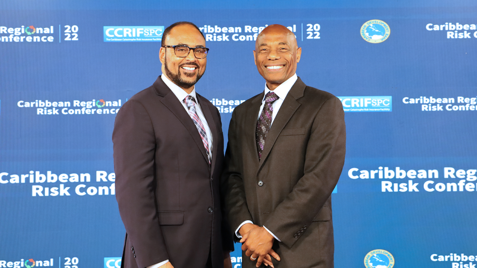 CDB President and CCRIF SPC CEO in dark suits with step and repeat backdrop behind him featuring conference logo
