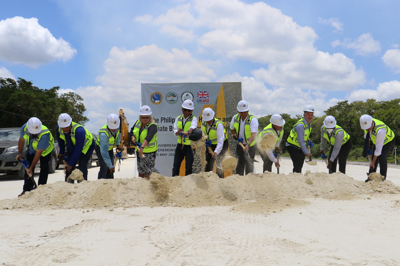 row of persons in reflector vests with shovels in hand, breaking ground