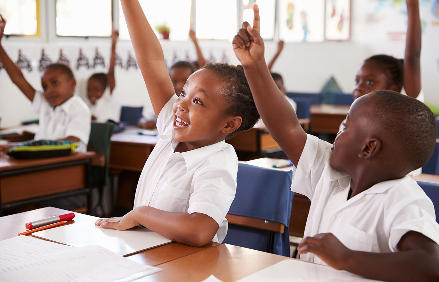 Kids raising hands during elementary school lesson, close up