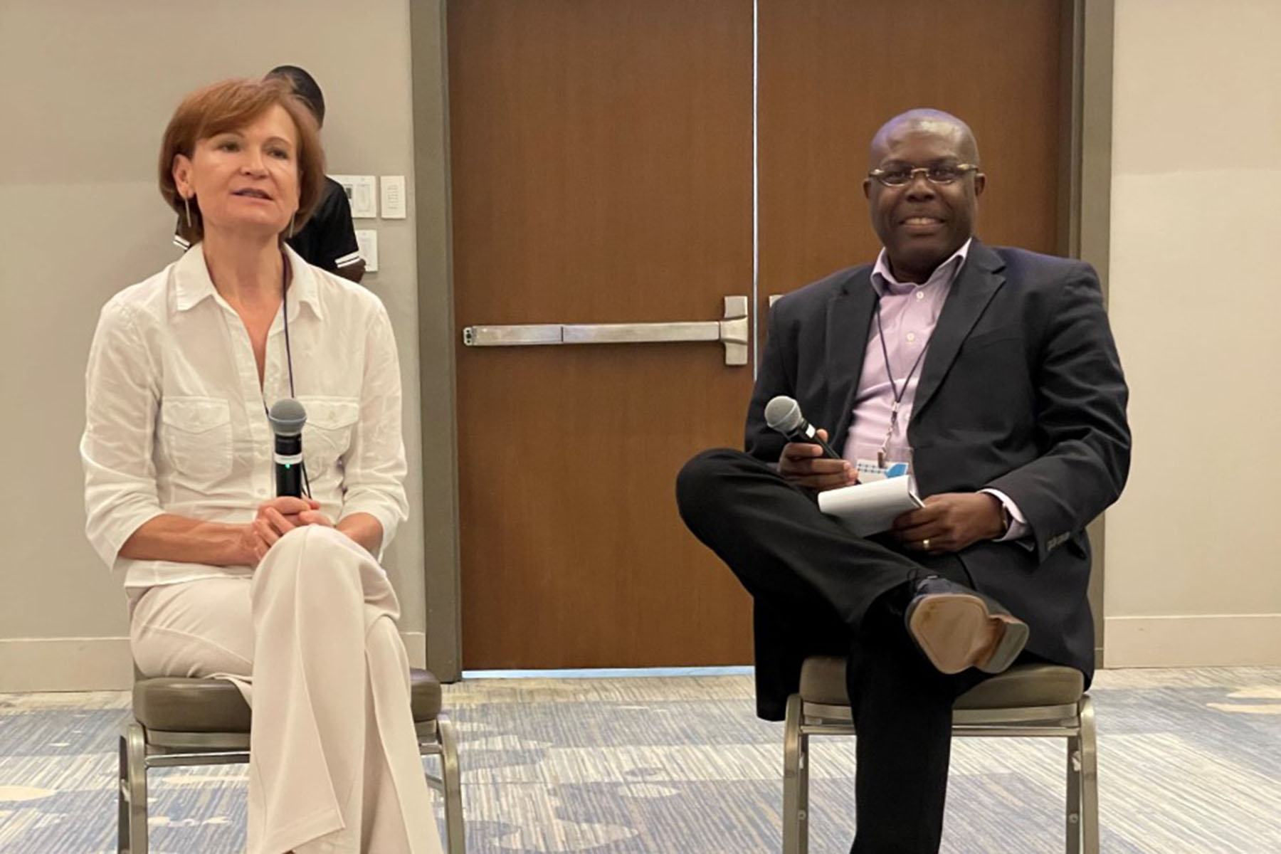 World Bank's Lilia Burunciuc dressed in white blouse and pants speaking with CDB's Isaac Solomon who is dressed in a black suit with white inside shirt