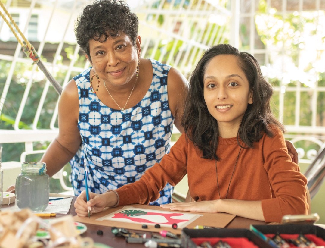 smiling lady artisan in brown sweater next to curly haired lady in blue and white check dress