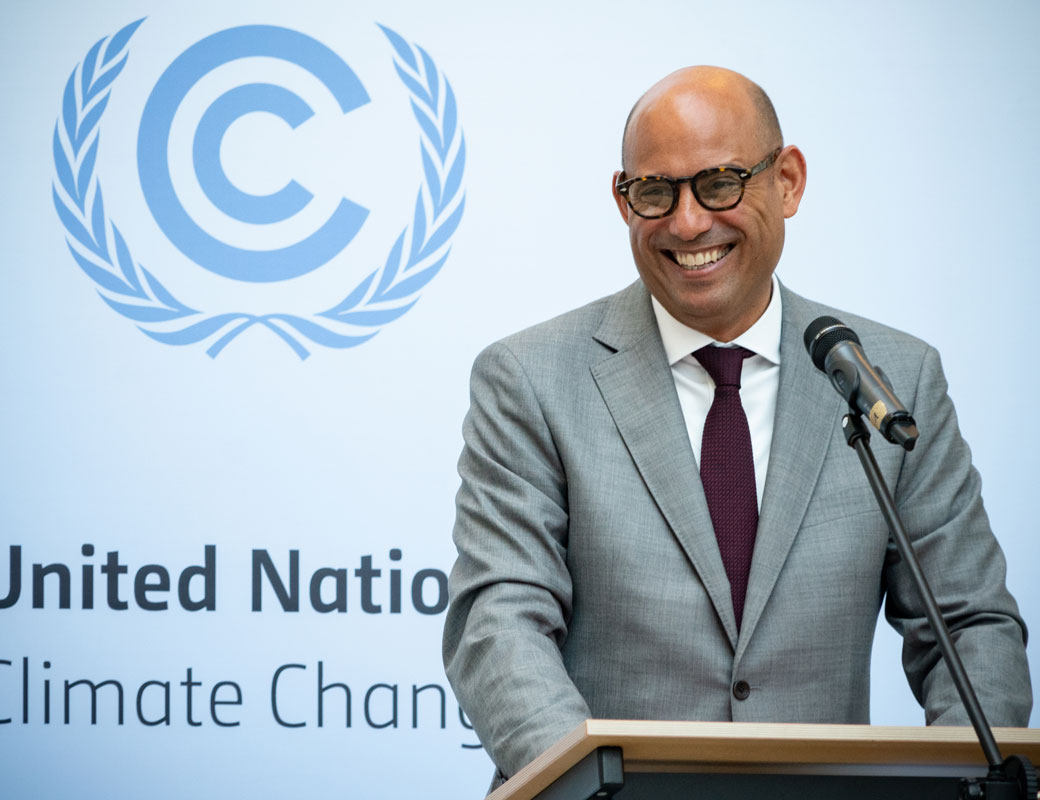 a smiling simon stiell wearing grey suit standing at lectern