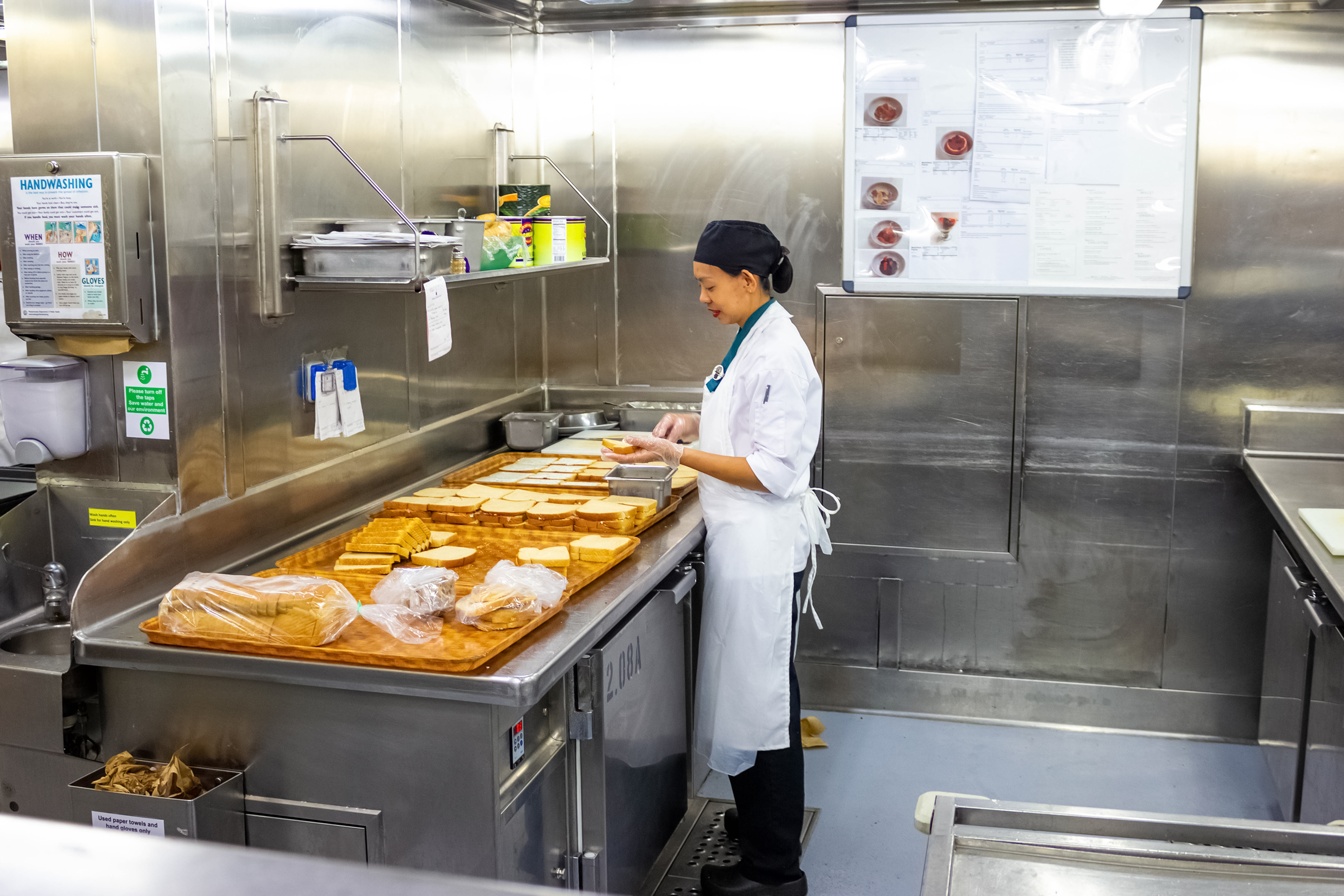 A woman stands in an industrial kitchen with bread making sandwiches