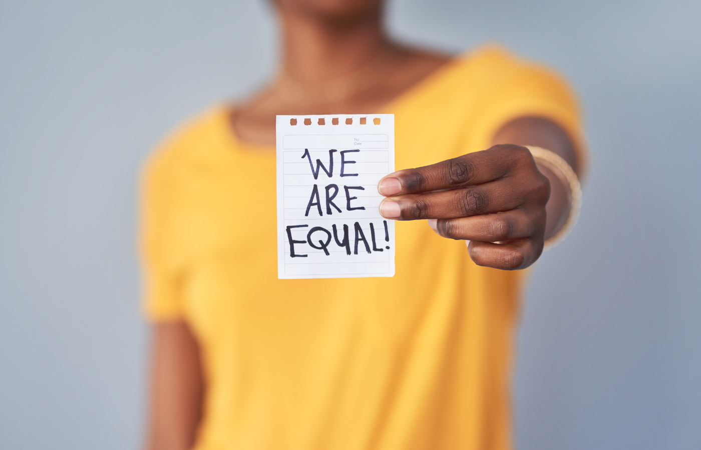 woman in yellow shirt holding hand outstretched with paper with the words 'We Are Equal'