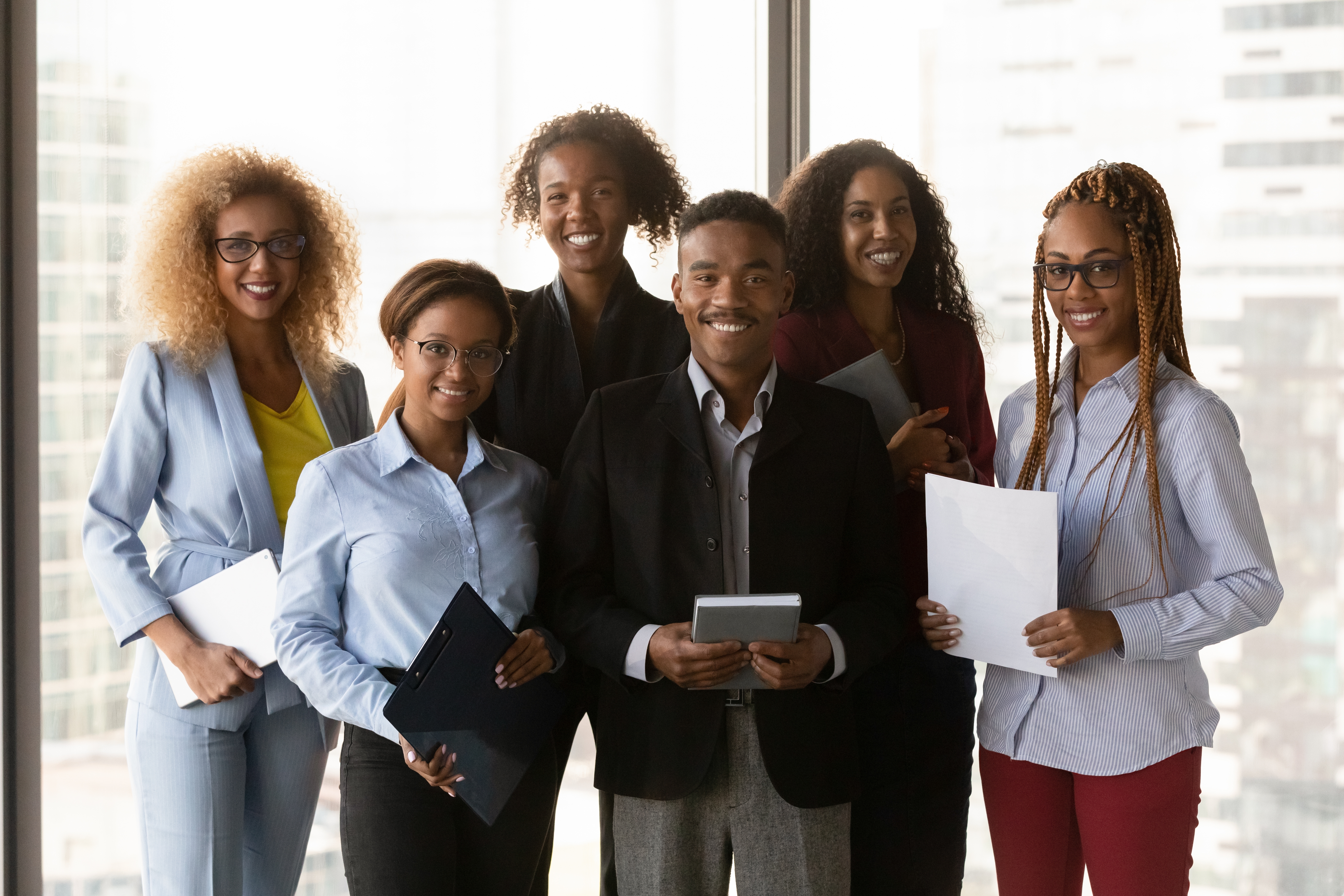 Six black professionals standing in a row holding papers and smiling