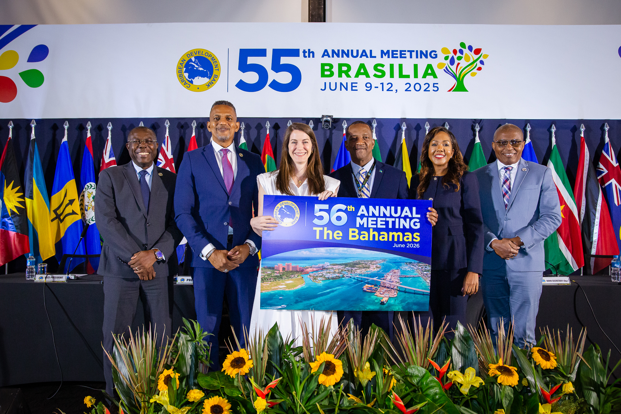 A photo of six people standing on a platform with an image of the beach in the background