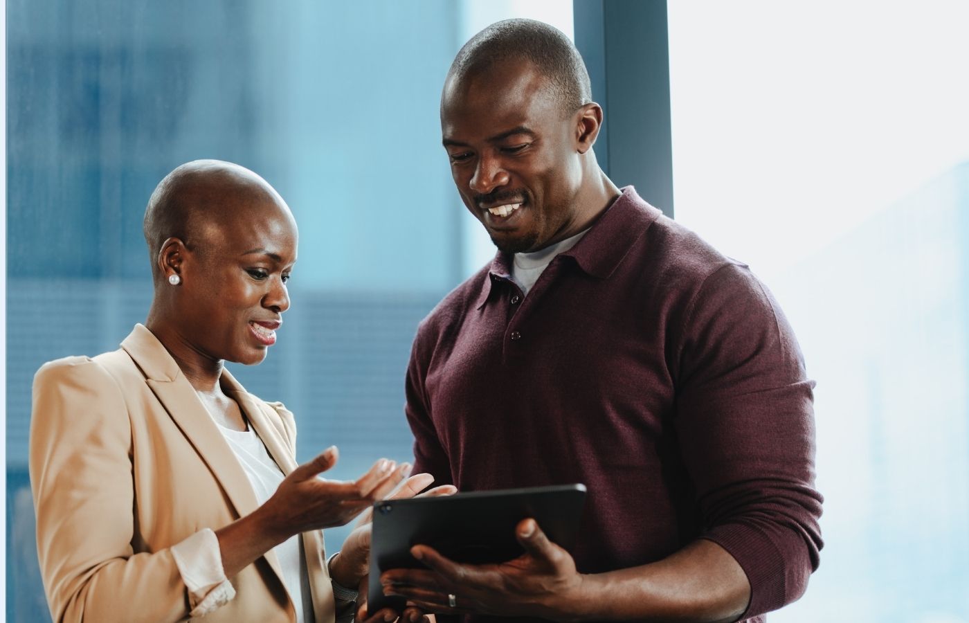 Black man and woman dressed professionally looking down at a tablet and smiling 