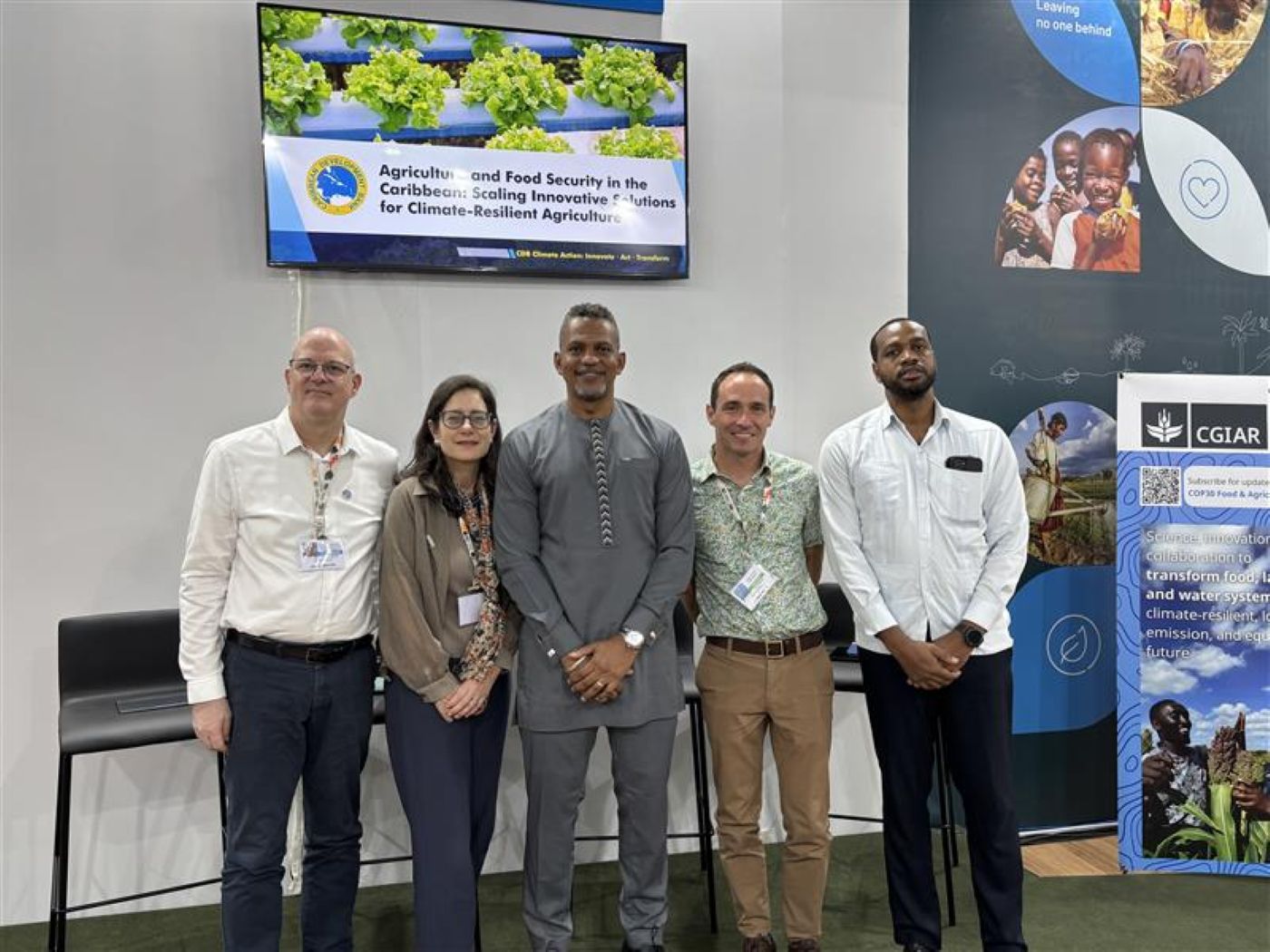 A group of five persons standing in a row looking ahead and smiling dressed professionally