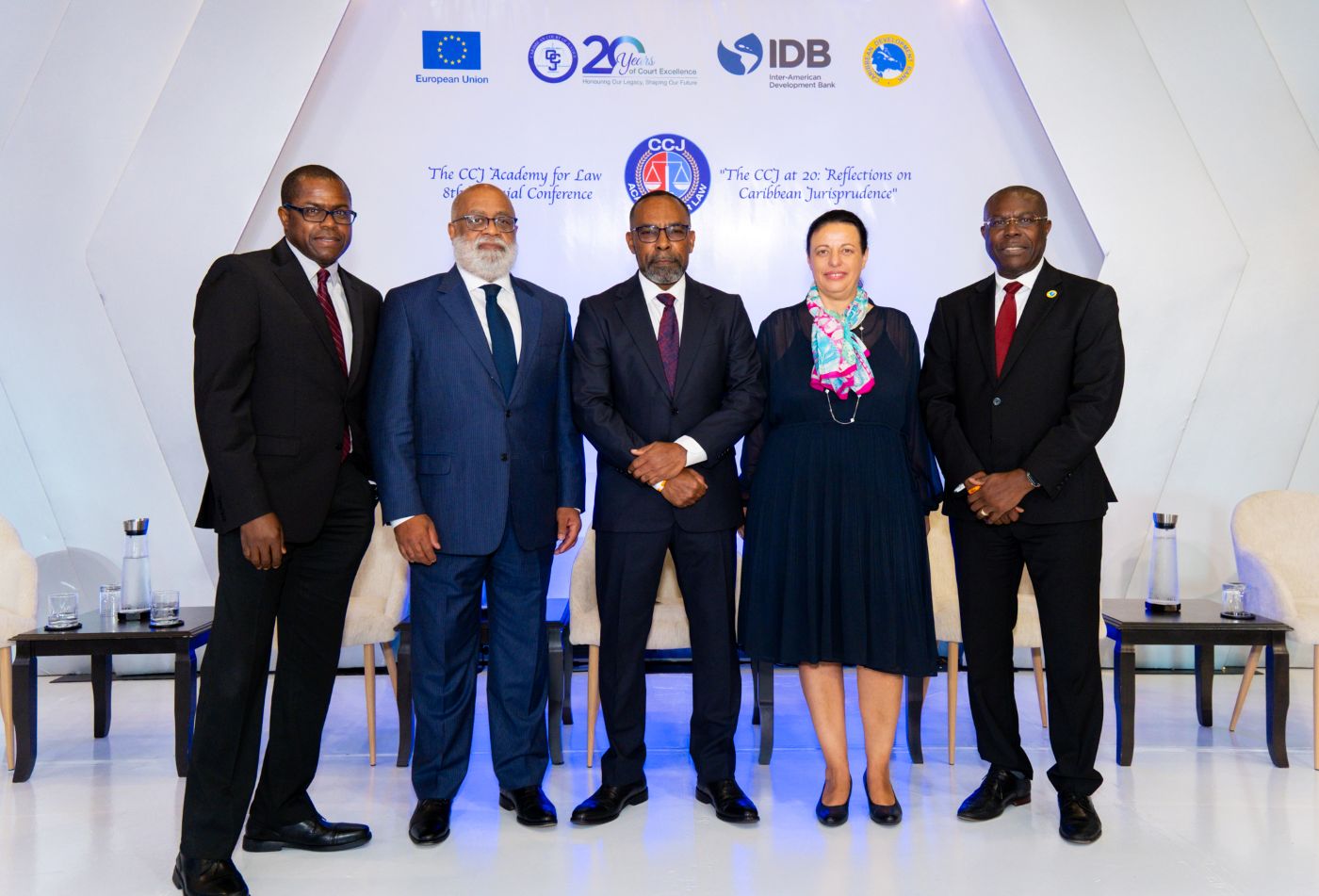 four gentlemen and one lady in dark business suits standing on a stage looking directly at camera