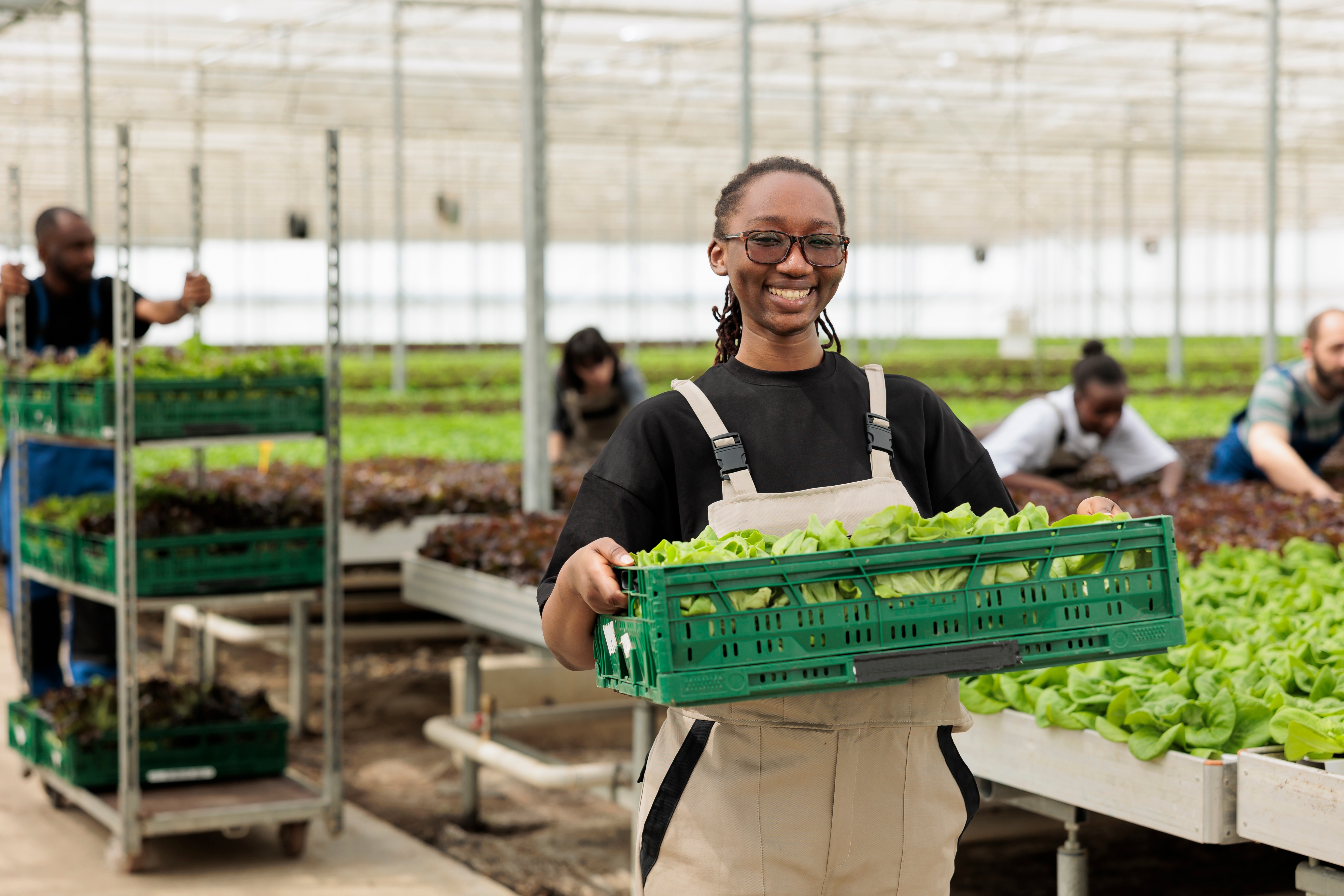 Woman farmer holds basket of produce in greenhouse.