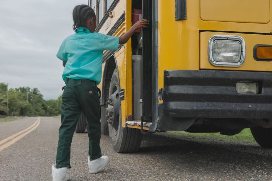 A young male student climbs onto a school bus.