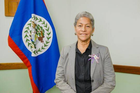 A woman stands next to a flag of Belize