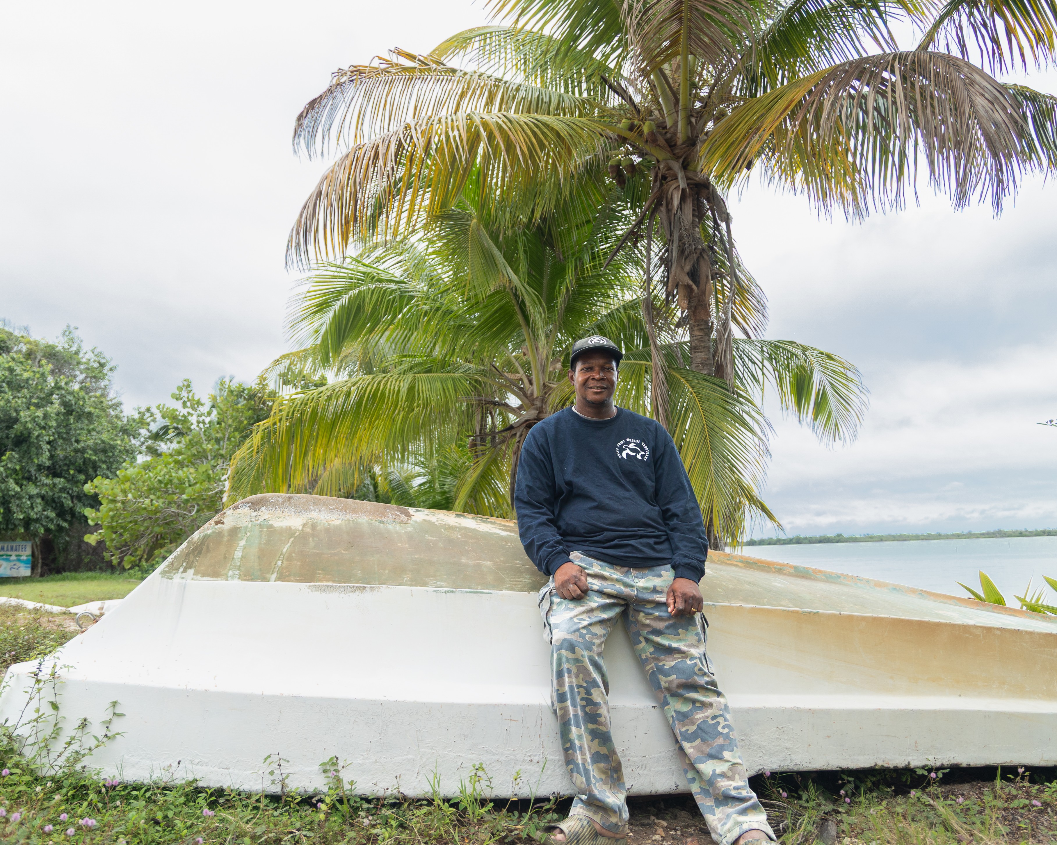 A black man leans against the hull of a boat.