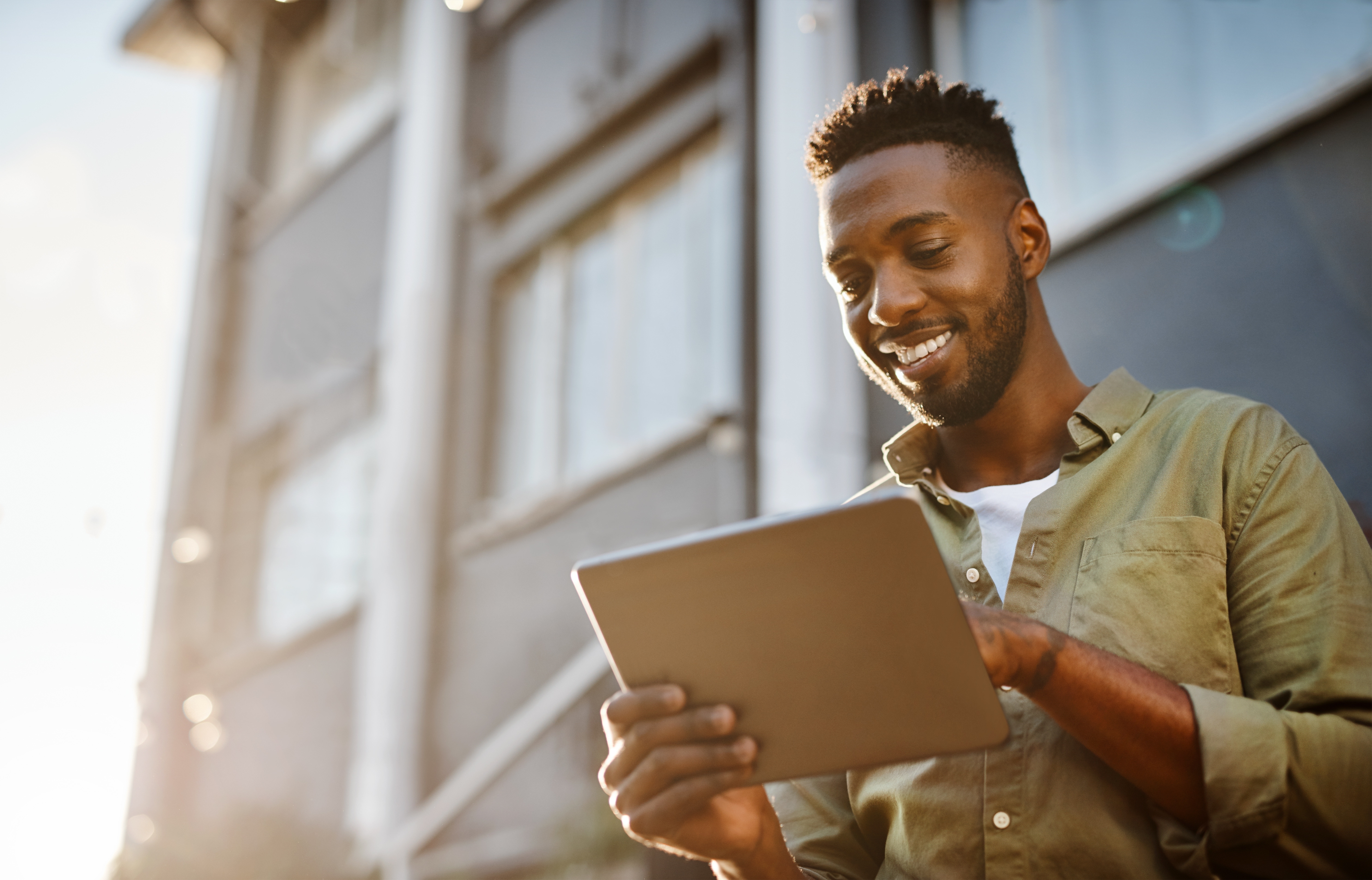 Young Caribbean man smiling and looking at his tablet.