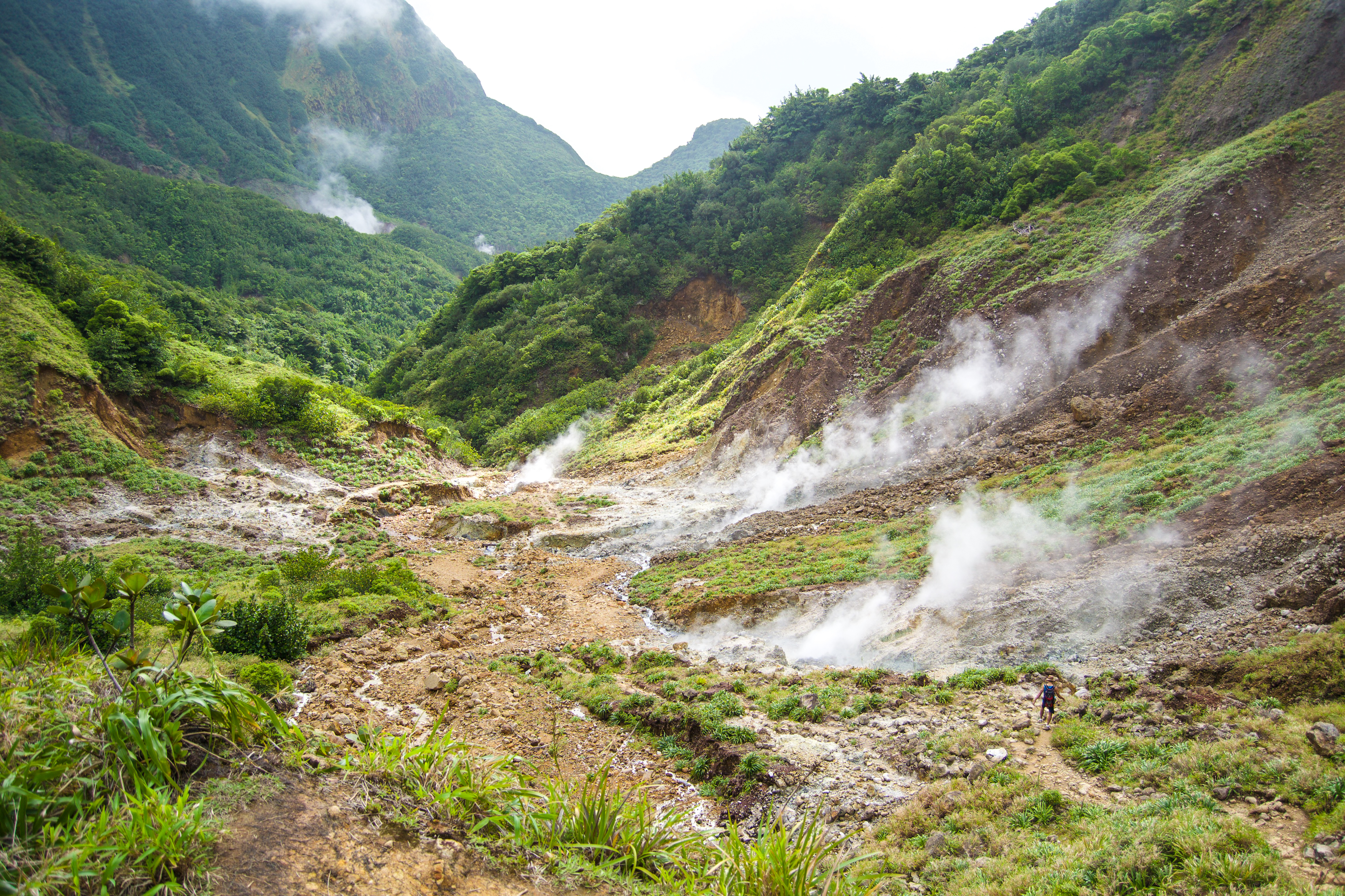 Clouds of geothermal steam rise from the ground in a mountainous area.