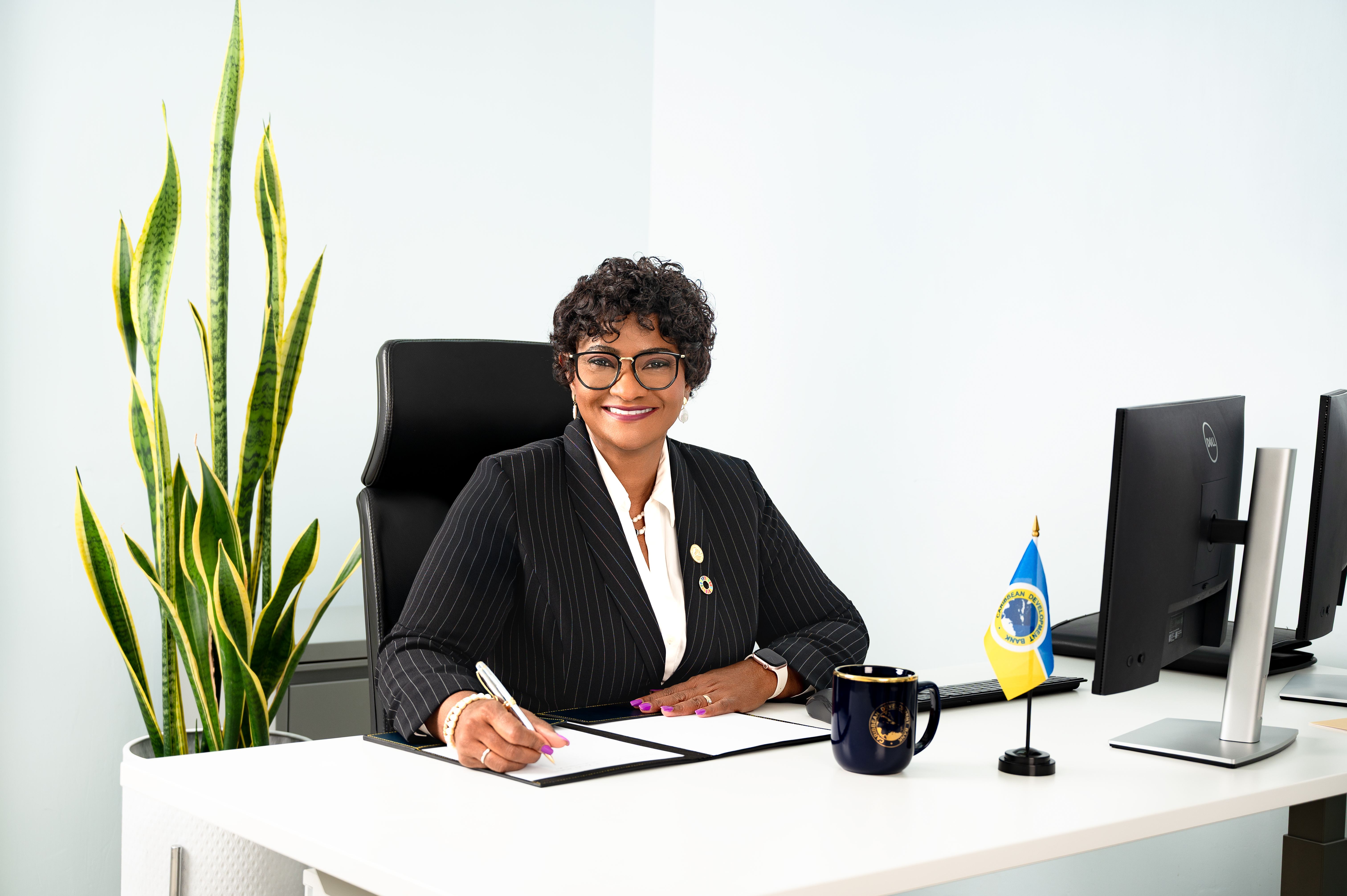 Lady sitting at a desk holding a pen in black and white business atire smiling 