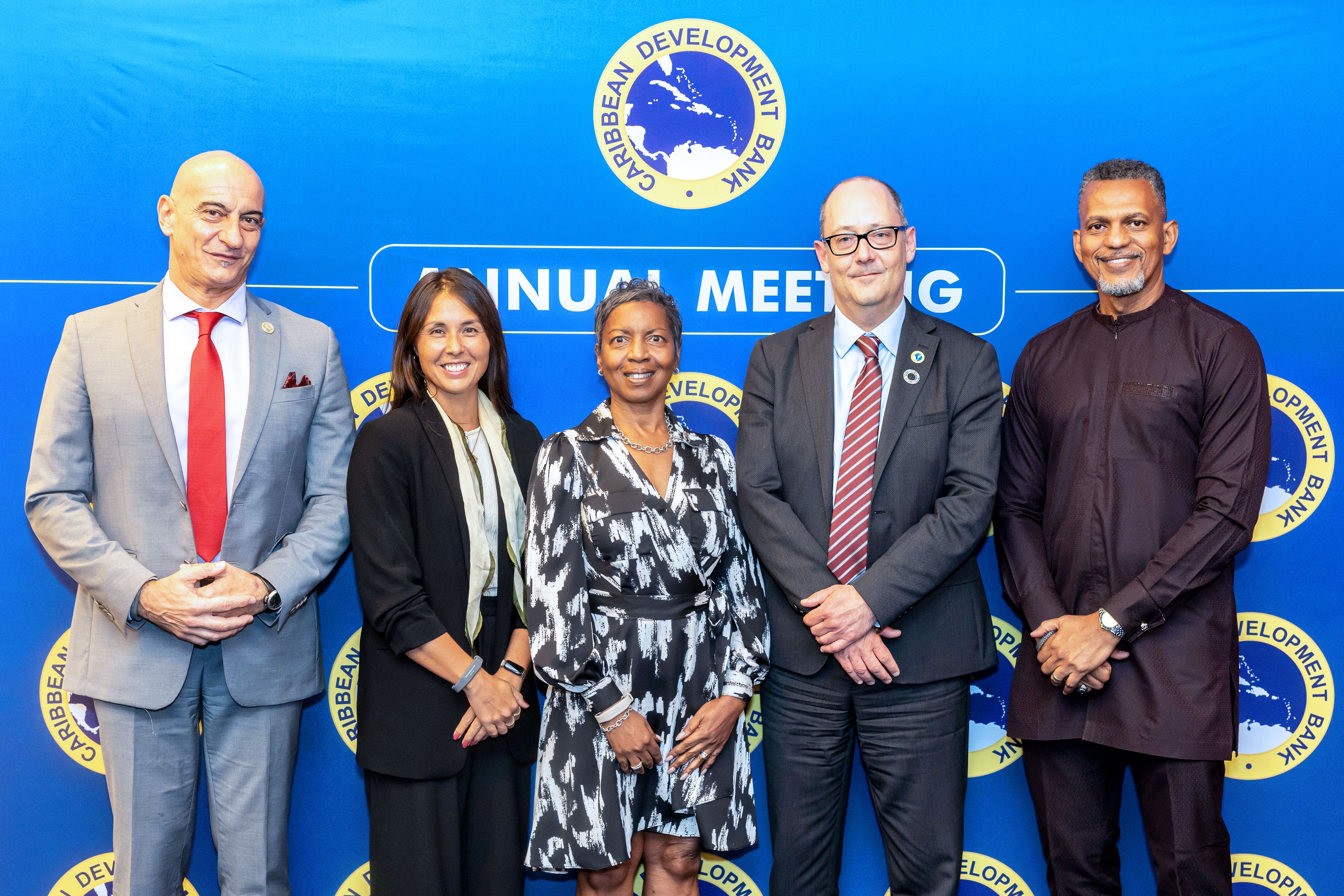 a group of five persons standing in a row in business attire in front of a colourful back drop two women three men