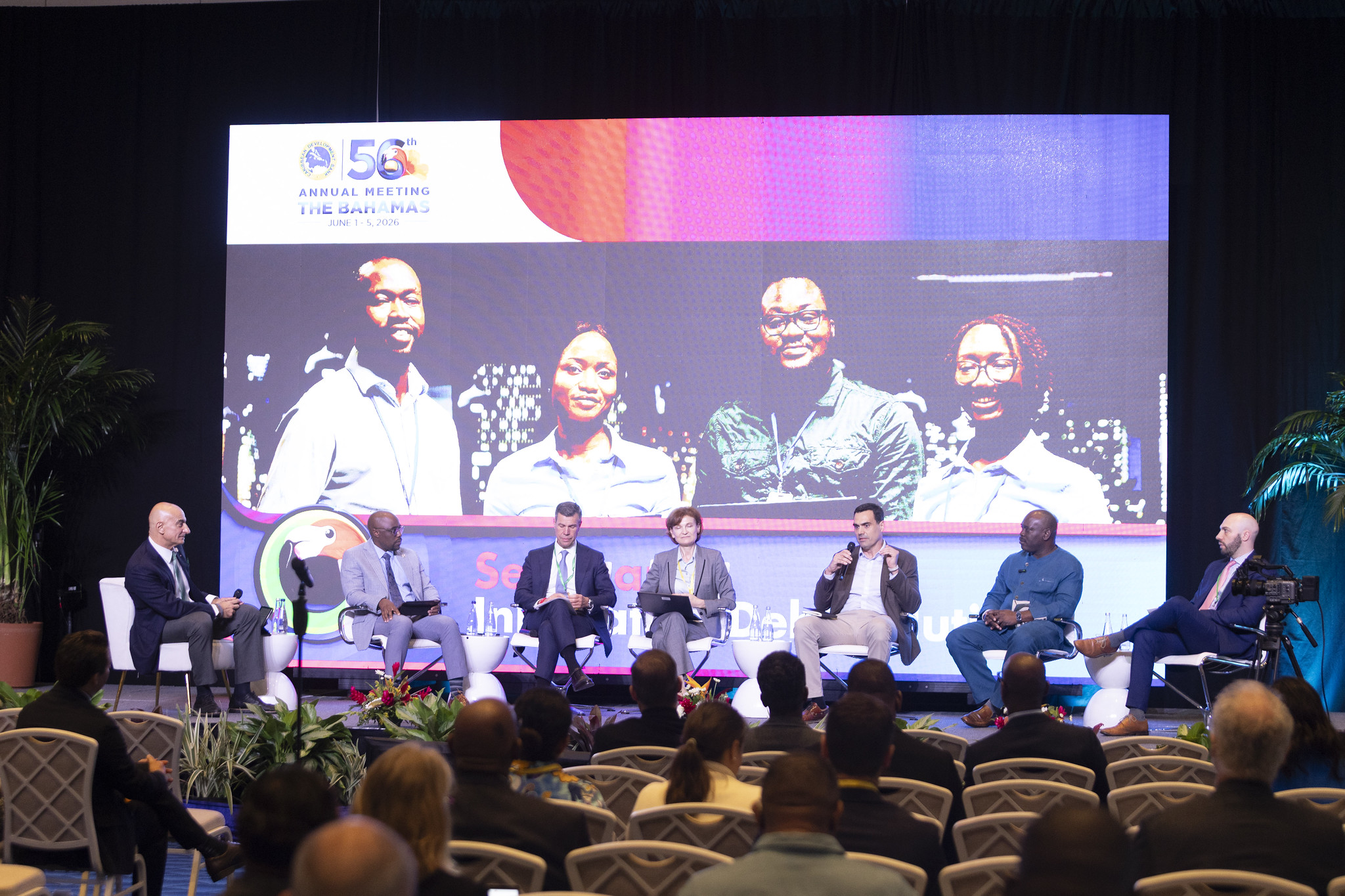 Group of panelists seated on stage in front of image of four people on screen