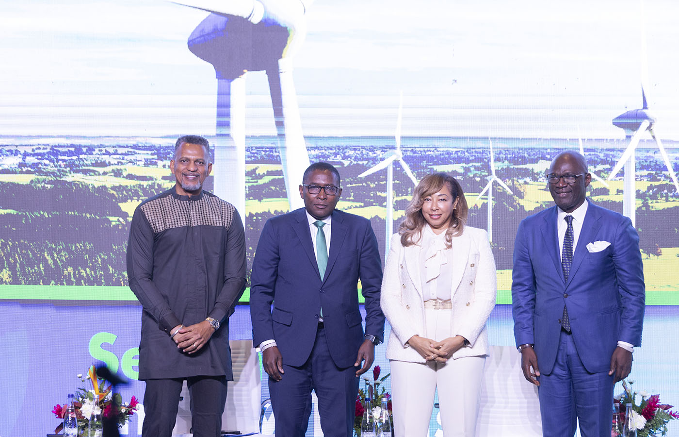Four speakers standing on a stage in front of a wind turbine backdrop at The Breakfast Exchange: A Climate Talk on the Global Economy