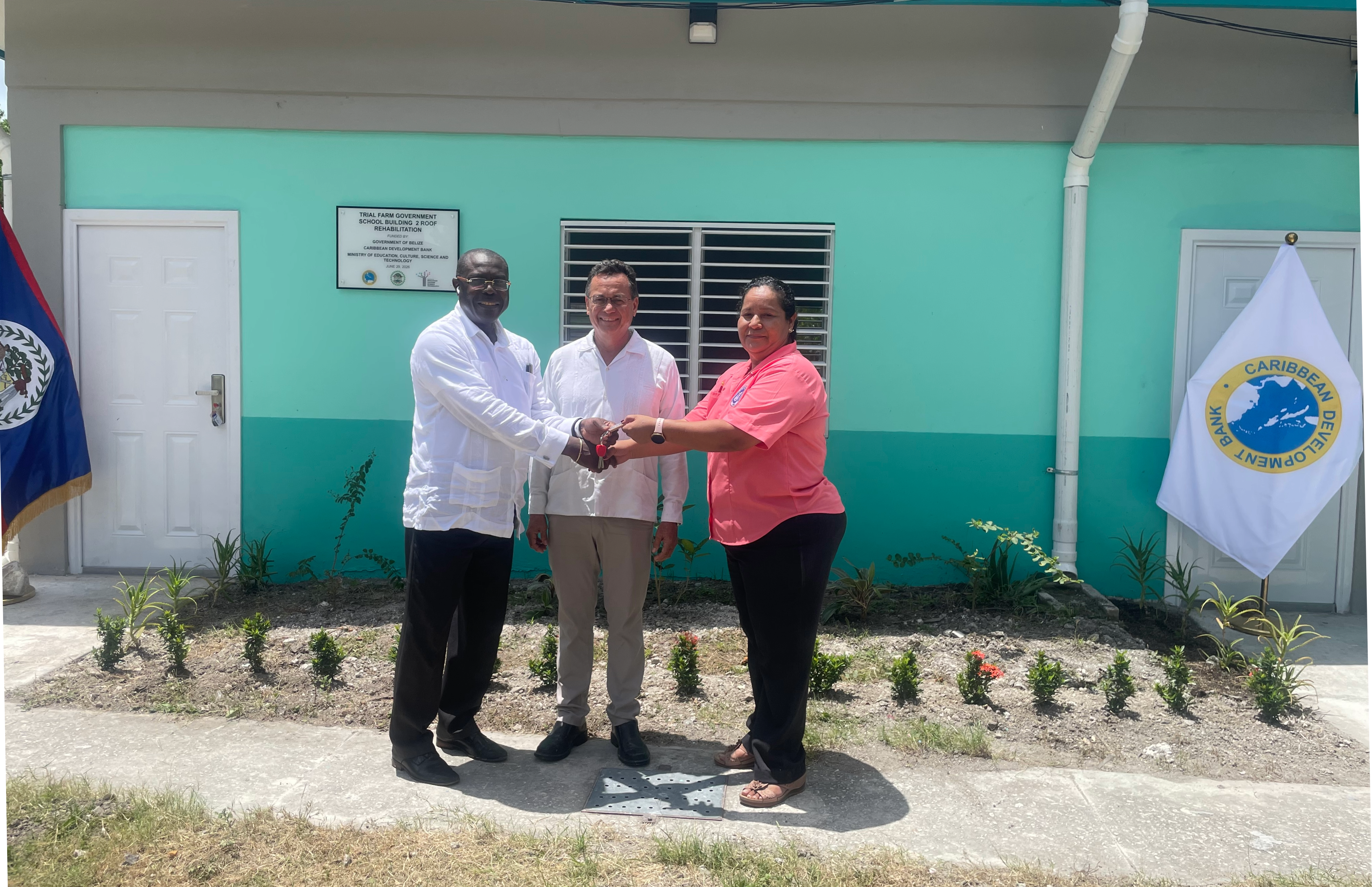 Two male officials hand over the keys to a female educator at a new school in Belize 