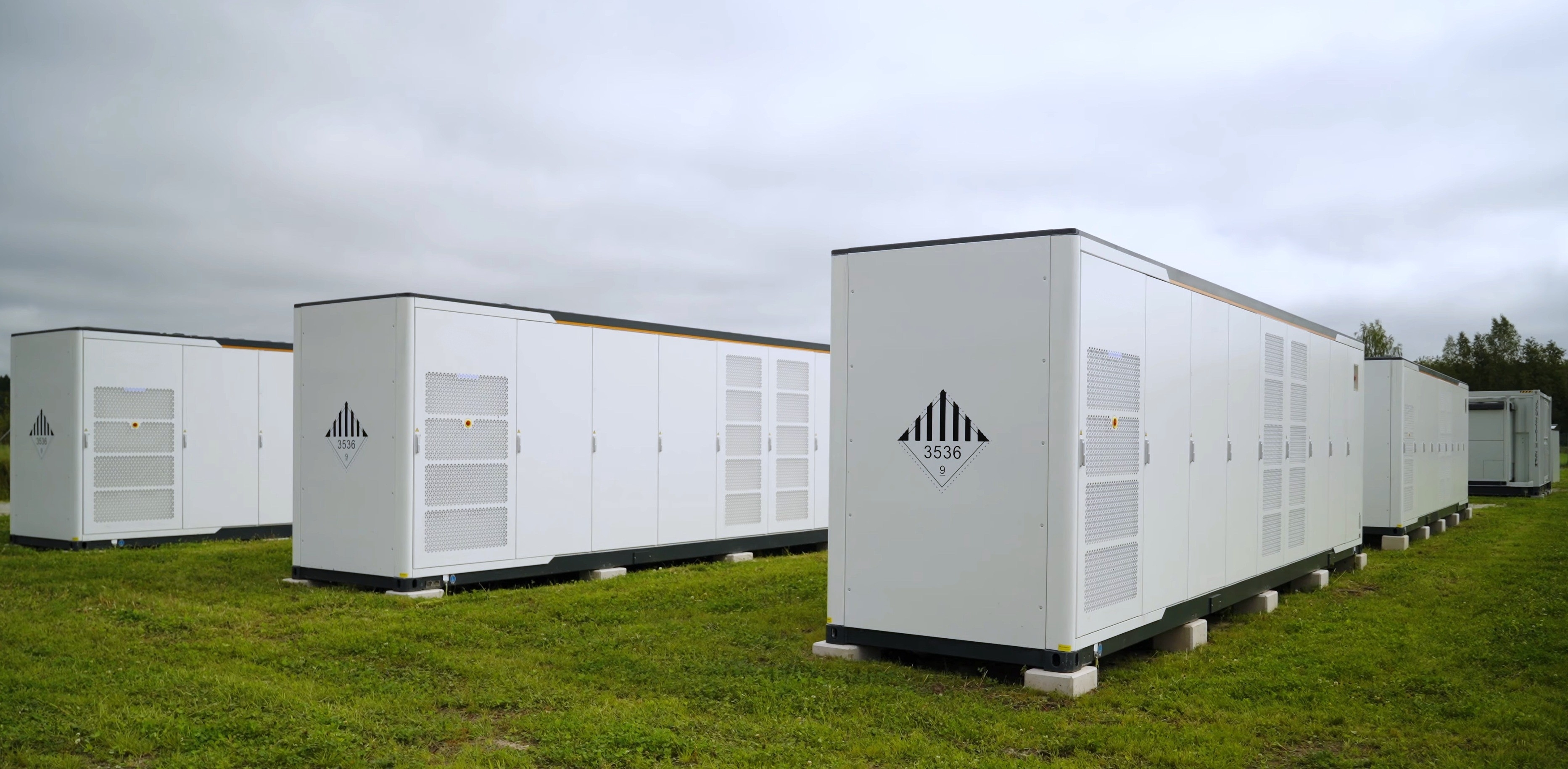 Row of three energy battery storage containers in a field.