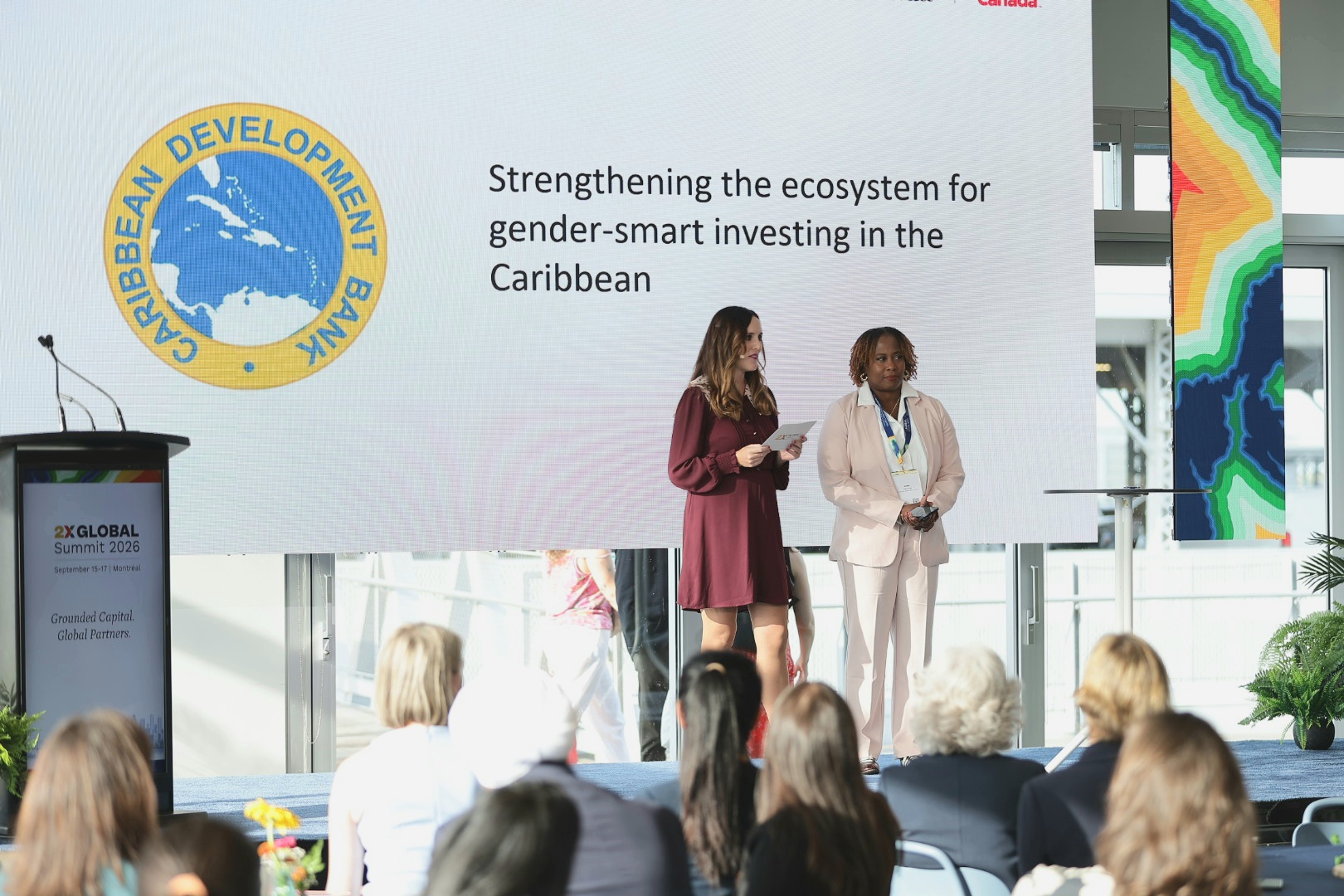Two women on stage with CDB logo and slogan behind