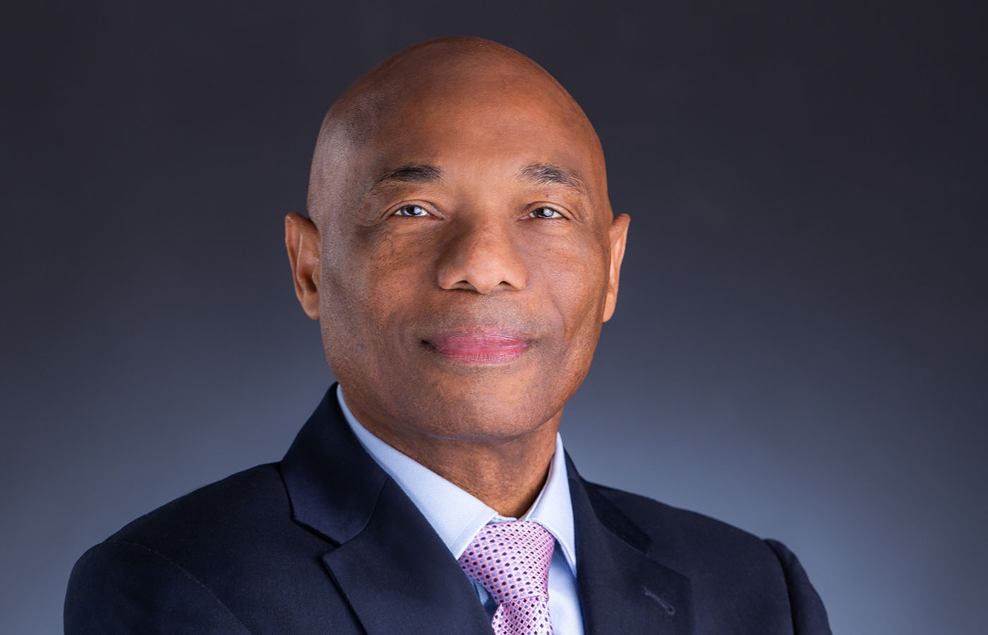 President Dr. Leon in dark suit with white shirt and patterned lilac tie