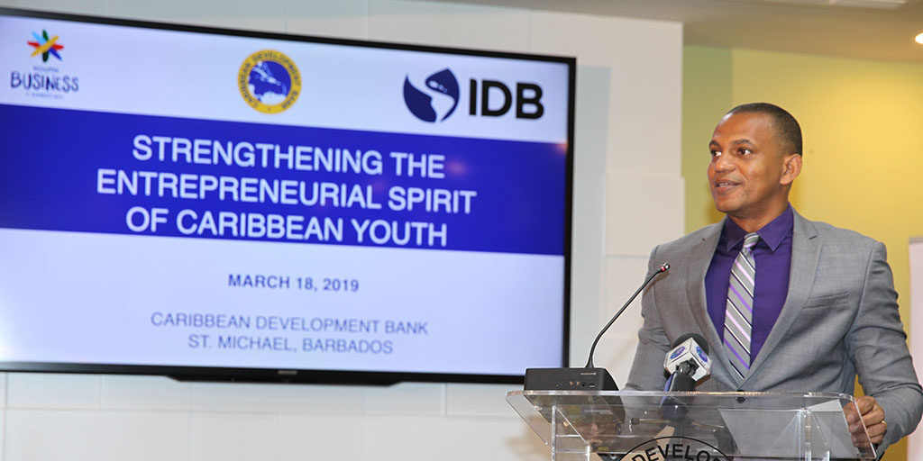 Daniel Best standing at lectern in grey suit with purple inside shirt