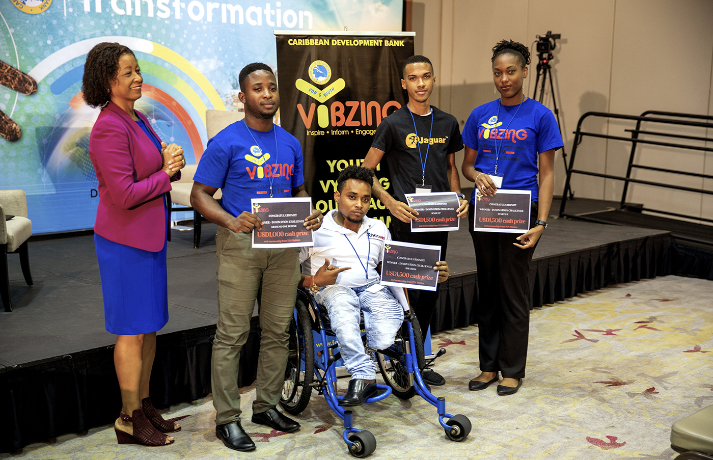 Four young people and woman standing in front of stage with certificates.