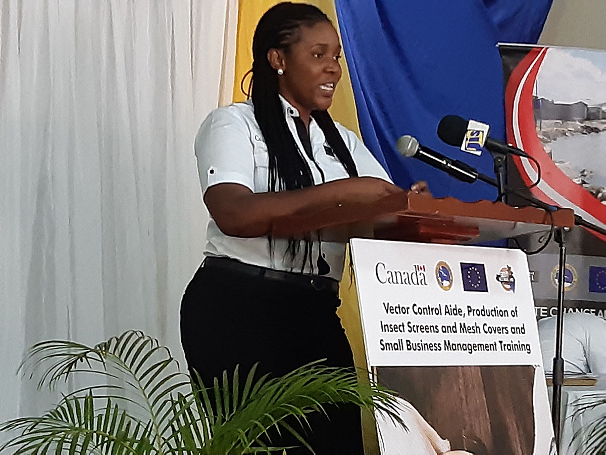 young woman with braids wearing a white shirt and black slacks standing at a wooden lectern