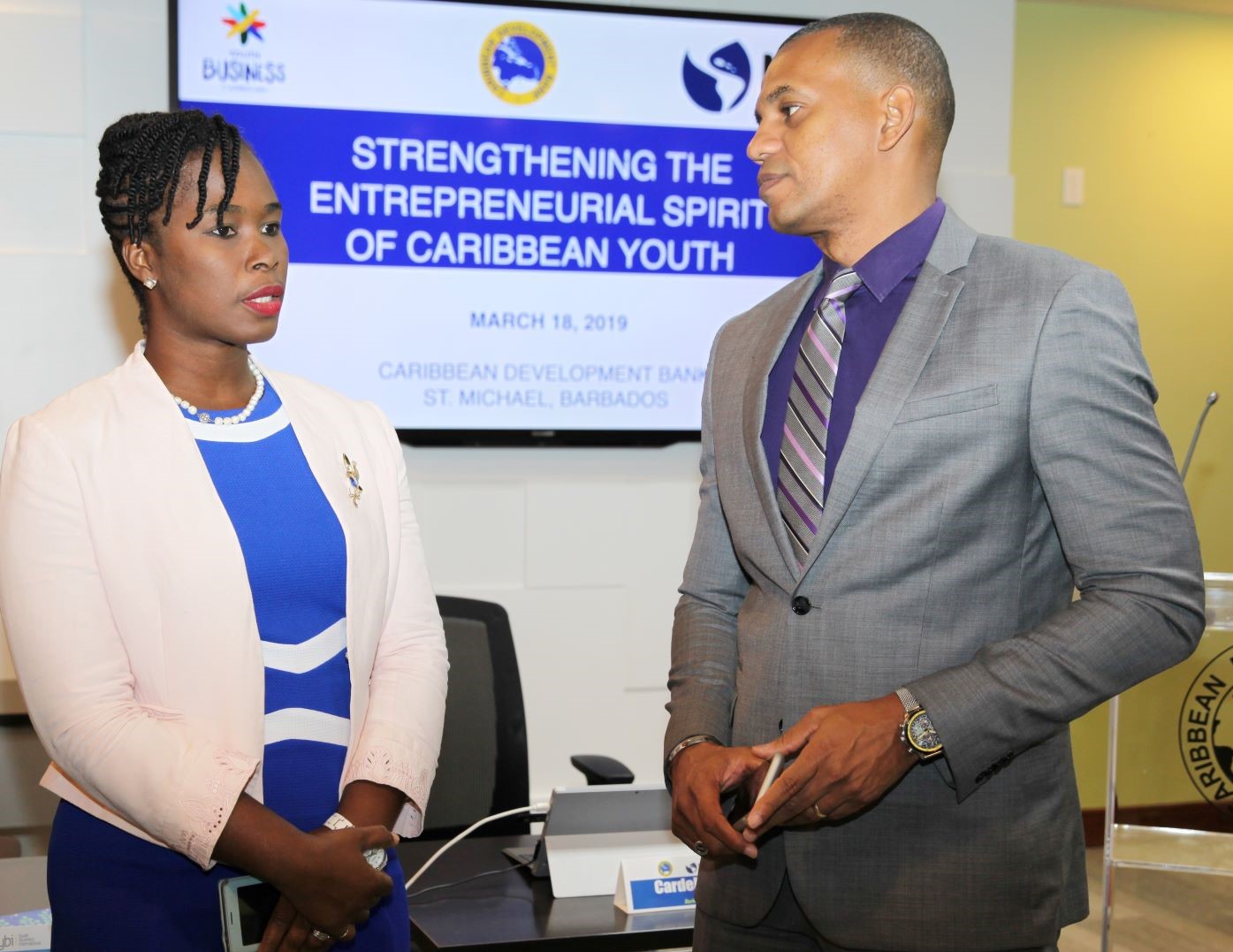 Cardell Ferguson in pink jacket and blue dress speaking with Daniel Best in grey suit and purple shirt