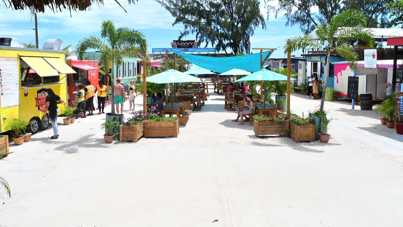 colourful beach stalls with white sand, customers and blue umbrellas, white sand and string lighting