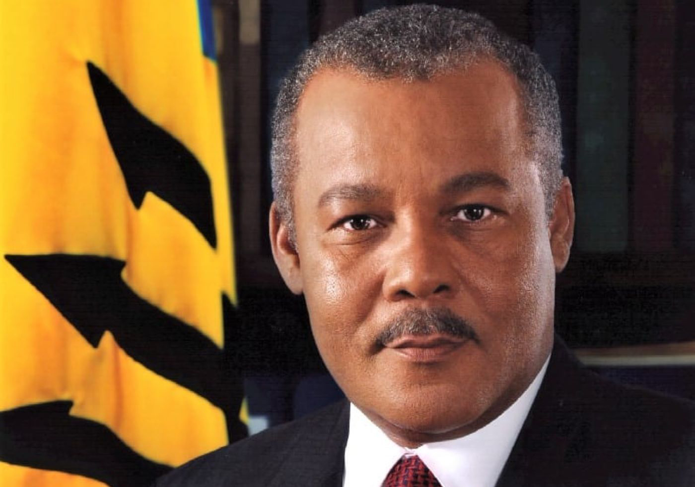 Photo of Prime Minister Owen Arthur with Barbados flag in background to left.