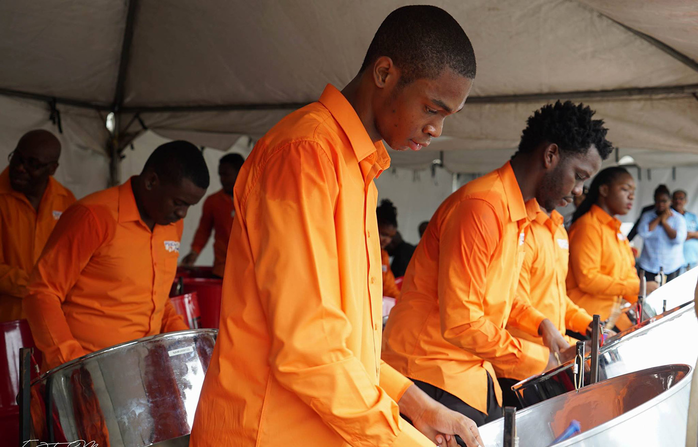 Men in orange shirts playing steelpan.