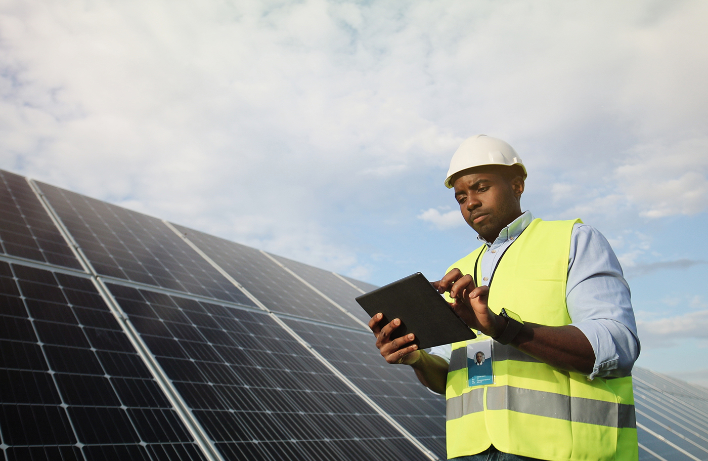 Technician in yellow jacket standing next to solar panels