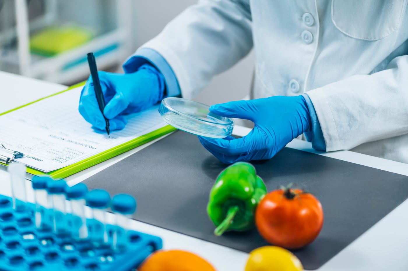 lab tech in white jacket and blue gloves with vegetables and vials on desk