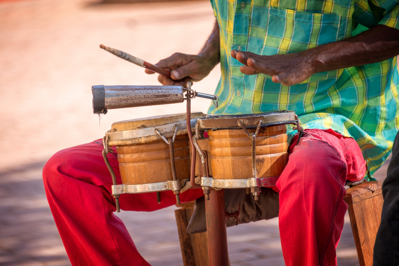 Man in green plaid shirt and red pants playing drums