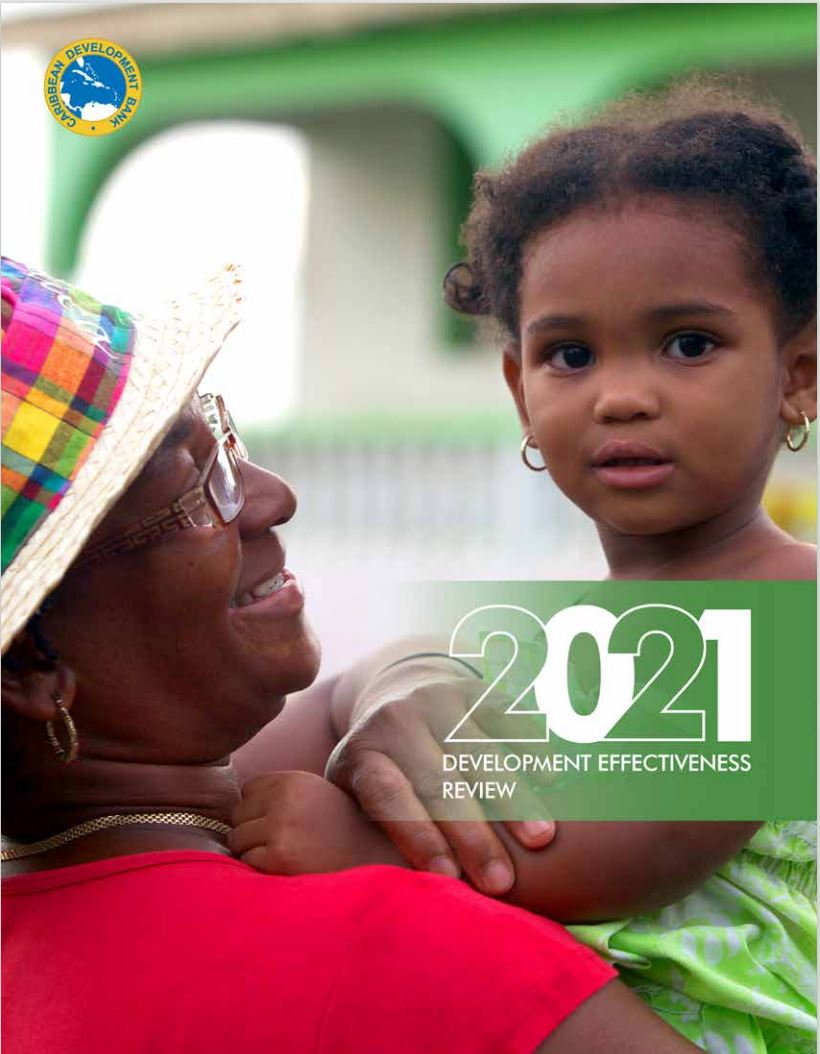 afro Caribbean grandmother in a read shirt and colourful hat holds a female toddler in her arms as toddler looks into the camera