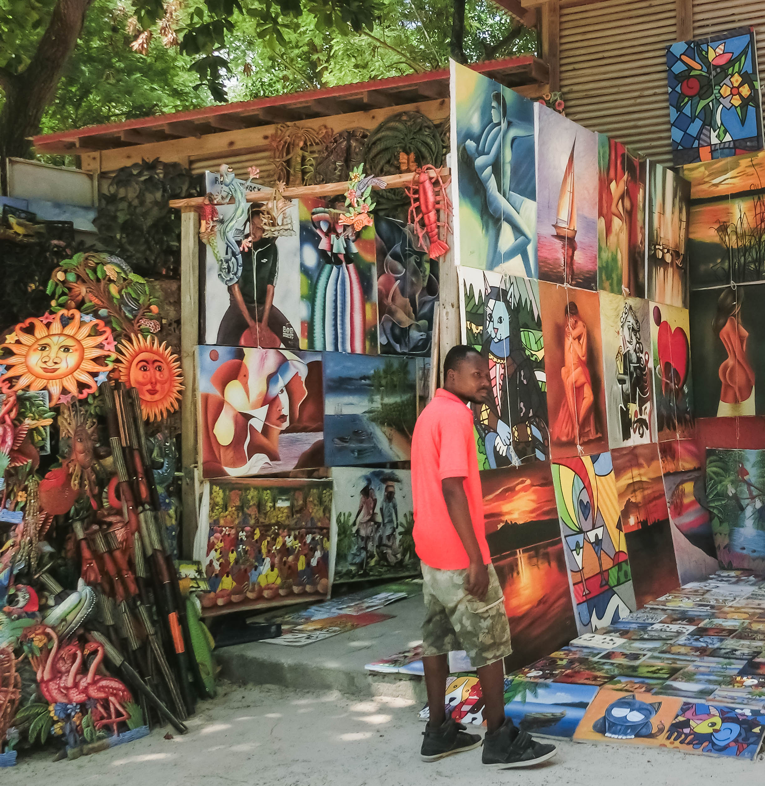 Art vendor stands by outdoor stall with several paintings hung up