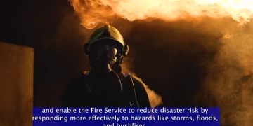 image of firefighter in full gear backlit by a fire