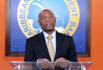 CDB President Dr Gene Leon at lectern with orange background and large CDB logo behind him.