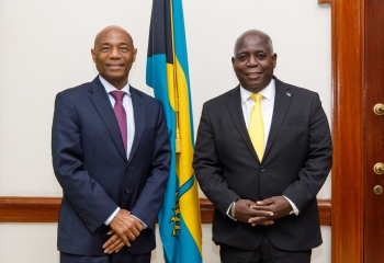 Dr. Gene Leon and the Honourable Philip Davis stand in front of The Bahamas flag