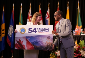 man handing over large signage board to woman on stage