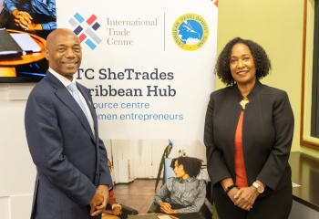 image of CDB President, Dr. Leon dressed in a dark business suit with white inside shirt standing next to ITC Executive Director, Pamela Coke-Hamilton,  who is dressed in a red dress with black business jacket.